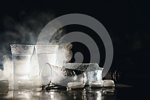 Close-up view of bottle and glasses of vodka standing isolated on black.