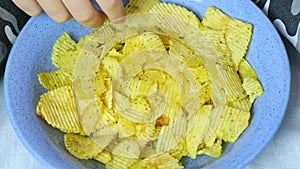 Close up view of a bowl full of crispy potato chips and a hand taking chips to eat