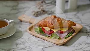 Close up view of breakfast meal with croissant sandwich ham, cheese on wooden plate and tea cup