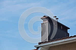 Close-up view of brick stone pipe covered with metal sheets and a black smoke box on roof. Ventilation pipe on roof of modern
