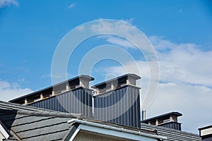 Close-up view of brick stone pipe covered with metal sheets and a black smoke box on roof. Ventilation pipe on roof of modern