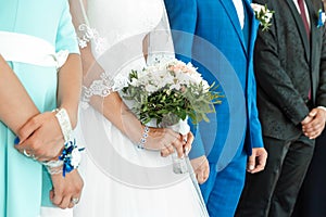 A close up view of a bride`s hands and bouquet with the bridal party in the background. Concept of marriage, family relationship,