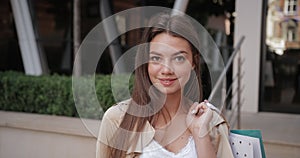 Close up view of brunnette millennial girl holding paper bag on her shoulder and smiling. Portrait of charming woman