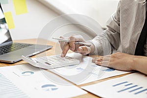 Close-up view A businessman using a calculator to calculate numbers on a company`s financial documents.