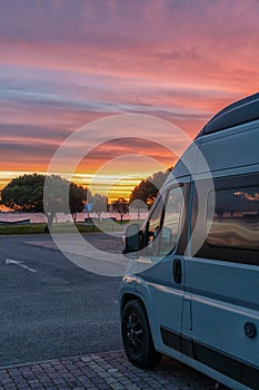 Close up view of a camper van parked at a beach parking lot under a beautiful sunset sky