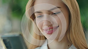 Close up view Caucasian blonde businesswoman 25s smiling woman use mobile gadget look at phone screen read messages in