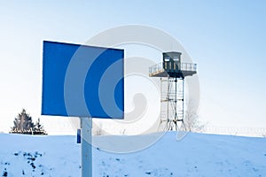 Close-up view of a caution banner, mock-up of a blue plate on an iron mesh fence against the surveillance tower. Closed area