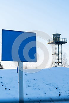 Close-up view of a caution banner, mock-up of a blue plate on an iron mesh fence against the surveillance tower. Closed area