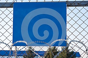 Close-up view of a caution banner, mock-up of a blue plate on an iron mesh fence with barbed wire. Closed area designation blank.