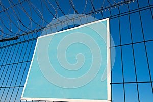 Close-up view of a caution banner, mock-up of a blue plate on an iron mesh fence with barbed wire. Closed area designation blank.