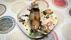 Close up view of `Cencaru Bakar Sumbat Sambal` in Malay or grilled fish half eaten on a white plate on table