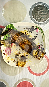 Close up view of `Cencaru Bakar Sumbat Sambal` in Malay or grilled fish half eaten on a white plate on table