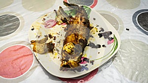 Close up view of `Cencaru Bakar Sumbat Sambal` in Malay or grilled fish half eaten on a white plate on table