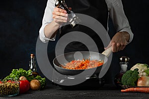 Close-up view of chef pours pepper into pan with frying vegetables for cooking soup on dark blue background. Backstage of