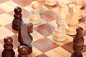 Close-up view of chess game with white and black log pieces on brown chessboard. Fight with horse and pawns