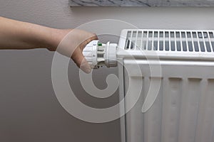 Close up view of child`s hand turning off thermostat on heating radiator to save energy.