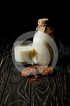 close up view of chocolate cookies, fresh milk in glass and bottle wrapped by paper on black background