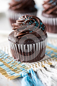 A close up view of a chocolate cupcake with chocolate frosting and blue sprinkles ready for eating.