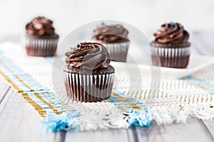 A close up view of a chocolate cupcake with chocolate frosting and other cupcakes in soft focus in behind.