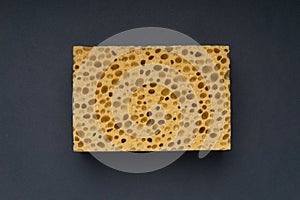 Close up view of cleaning sponge, mesh structure pattern on black surface. Yellow sponge close-up.