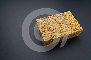 Close up view of cleaning sponge, mesh structure pattern on black surface. Yellow sponge close-up.