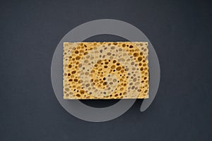 Close up view of cleaning sponge, mesh structure pattern on black surface. Yellow sponge close-up.