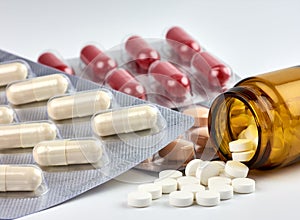 Close-up view of colorful pills and drugs spilled from a brown medicine bottle, on a blurred white background