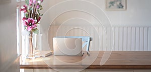 Close-up view of comfortable workplace with mock up laptop computer, office supplies and pink flower vase on wooden table