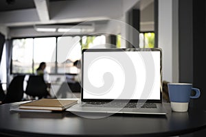 Computer laptop with blank screen, coffee cup and notebook on black office desk.