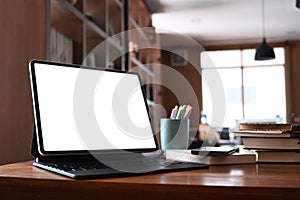 Close up view of computer tablet with blank screen and books on wooden desk in library.