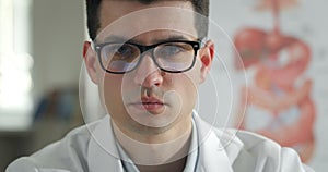 Close up view of concentrated male doctor looking to camera in medical office. Portrait of serious young man in white
