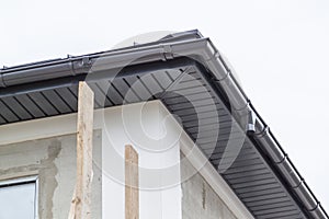 close-up view of corner of house with a gray roof and plums and filing of roof overhangs with soffits of house under construction