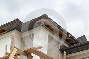 close-up view of corner of house with a gray roof and plums and filing of roof overhangs with soffits of house under construction