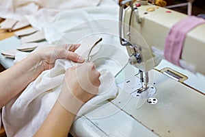 Close up view of cropped female hands sewing white fabric on professional manufacturing machine