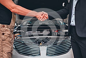 Close up view cropped shot, of a side profile view of businessman in a classy suit shaking arm of a mechanic, near the hood of his