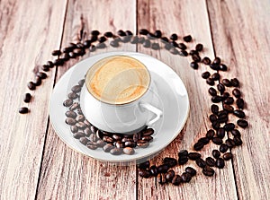 Close-up view of a cup of hot coffee on wooden rustic table with spilled coffee beans