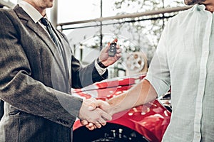 Close up view of dealer giving key to new owner and shaking hands in auto show or salon