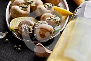 Close up view of delicious cooked escargots with lemon slices near white wine.