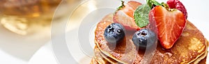 Close up view of delicious pancakes with honey, blueberries and strawberries, panoramic shot