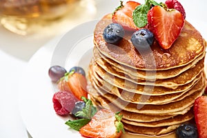 Close up view of delicious pancakes with honey, blueberries and strawberries on plate on white surface