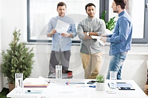 Close-up view of documents and business charts on desk and businessmen standing behind