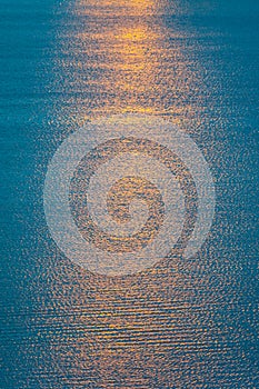 A dramatic orange sun way of reflections in deep blue water