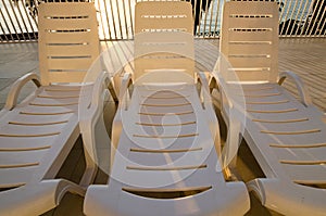 Close-up view of empty chaise lounges near swimming pool. Palm trees with blue sea in the background