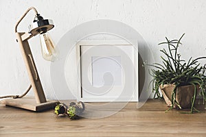 close up view of empty photo frame, table lamp and plant in flowerpot