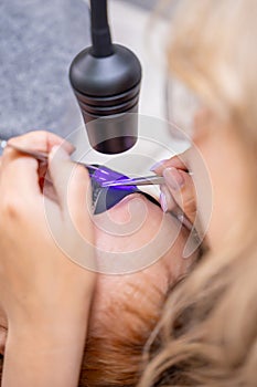 Close up view of eyelash extension procedure using ultraviolet lamp in modern beauty salon. Innovative lash enhancement photo