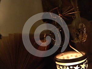 Close up view of a fairy sitting on a moon metal candle rotation carousel with stars shapes lit, in front of an open book , photo