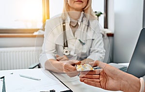 Close up view of female doctor`s hand giving pills in blister to female patient in clinic