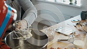 Close-up view of female hand putting the batter in the bowl. Young woman blending ingredients, using mixer for this.