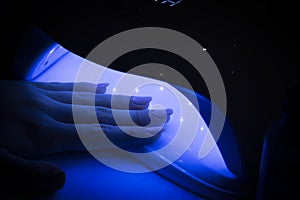 Close-up view of female hands with fresh beautiful modern manicure gel polish. A woman puts her hand into a UV LED lamp to cure