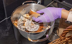 Close-up view of female hands in rubber gloves cleaning mushrooms in kitchen sink.